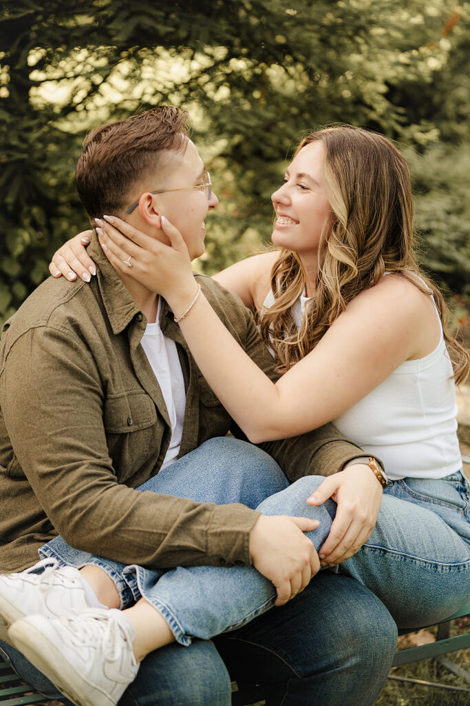 engaged couple sitting on bench smiling at each other 